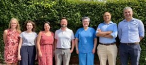 Picture of the seven GP Partners stood outside in the sun in front of a hedge.